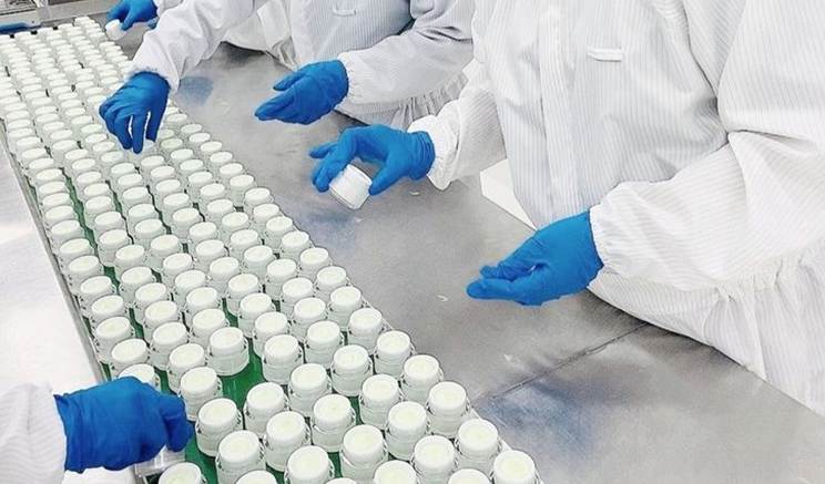 This may contain: three people in white lab coats and blue gloves are working on an assembly line with bottles