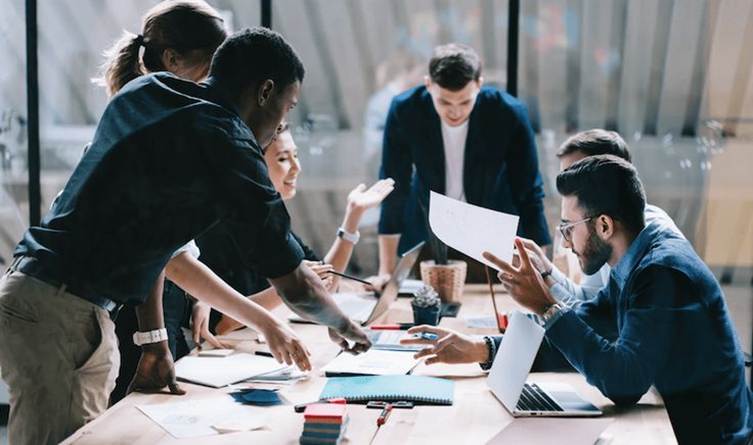 This may contain: a group of people sitting around a table with laptops and papers in front of them